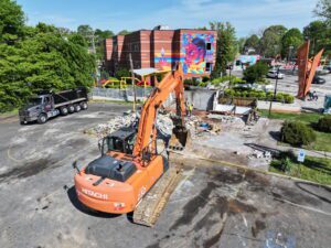 Excavator demolishing a commercial building at Johnson C. Smith University in Charlotte, North Carolina, with demolition debris, work crews, and haul trucks on site as JCE, Inc. completes structural demolition.