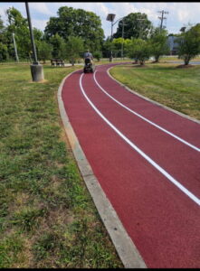 Curved red rubberized walking and running trail with fresh white lane striping in a landscaped public park.