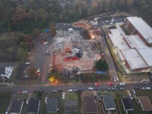 Aerial drone view of the Bruns Academy demolition project in Charlotte, North Carolina, showing a demolished school building, heavy demolition equipment, sorted debris piles, recycling operations, perimeter fencing, and adjacent school buildings as JCE, Inc. completes commercial demolition and site clearing.