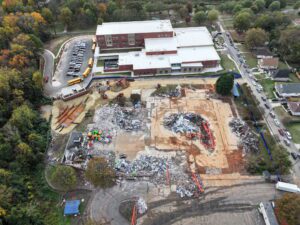 Aerial drone view of the Bruns Academy demolition project in Charlotte, North Carolina, showing a demolished school building, heavy demolition equipment, sorted debris piles, recycling operations, perimeter fencing, and adjacent school buildings as JCE, Inc. completes commercial demolition and site clearing.